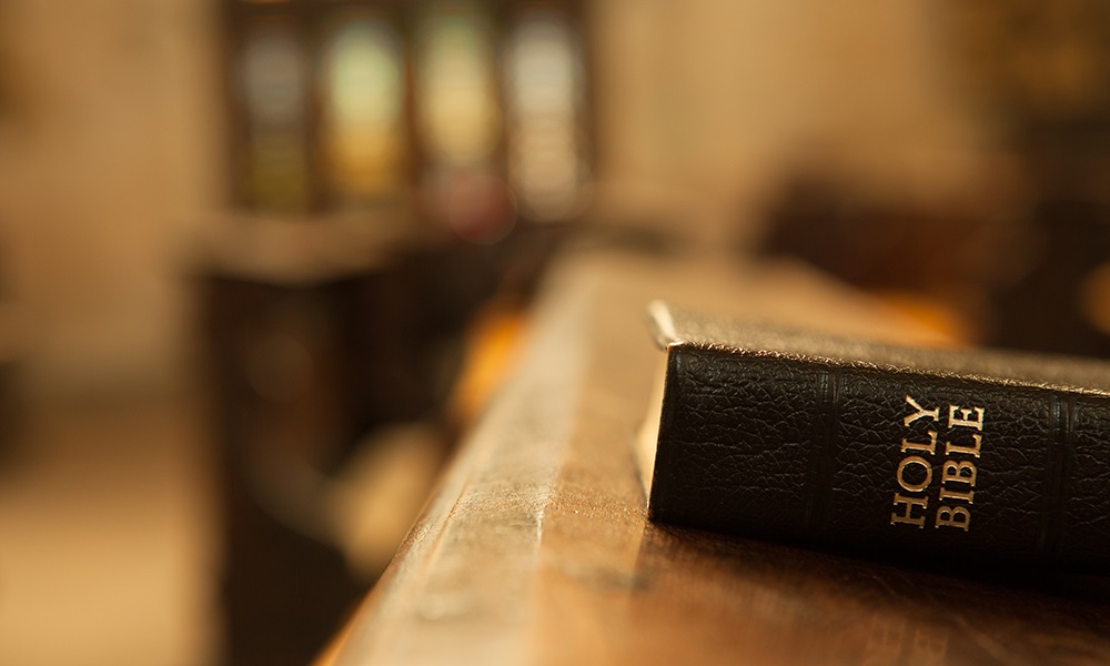 A Holy Bible resting on a wooden table inside a church.